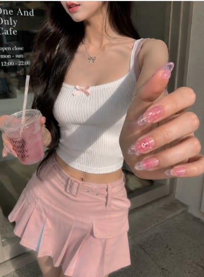 Young woman in a pastel pink outfit showing glossy 3D gummy bear jelly nails in close-up sunlight
